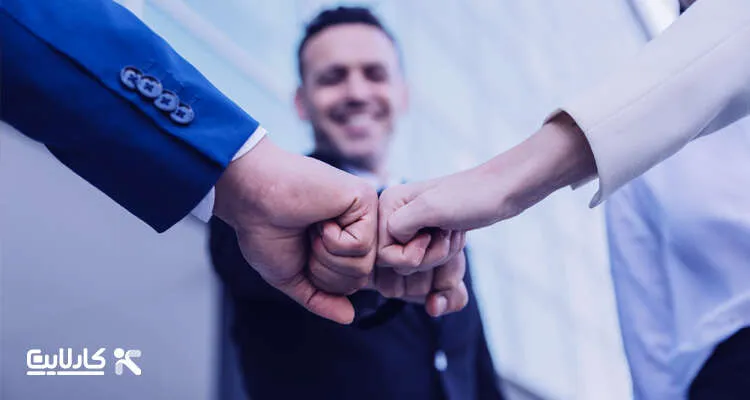 سه همکار در محیط کاری با ضربه مشت به یکدیگر، نماد همکاری و همدلی و بهبود ارتباطات